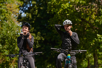 Image showing A blissful couple, adorned in professional cycling gear, enjoys a romantic bicycle ride through a park, surrounded by modern natural attractions, radiating love and happiness