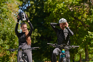 Image showing A blissful couple, adorned in professional cycling gear, enjoys a romantic bicycle ride through a park, surrounded by modern natural attractions, radiating love and happiness