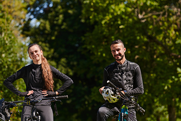 Image showing A blissful couple, adorned in professional cycling gear, enjoys a romantic bicycle ride through a park, surrounded by modern natural attractions, radiating love and happiness