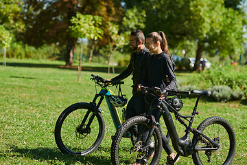 Image showing A blissful couple, adorned in professional cycling gear, enjoys a romantic bicycle ride through a park, surrounded by modern natural attractions, radiating love and happiness