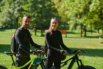 Image showing A blissful couple, adorned in professional cycling gear, enjoys a romantic bicycle ride through a park, surrounded by modern natural attractions, radiating love and happiness