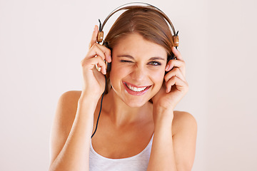 Image showing Woman, portrait and wink with headphones in studio for music, audio subscription or streaming multimedia album on white background. Happy model, blink and listening to podcast, hearing sound or radio