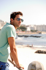 Image showing Thinking, fashion and man by ocean in city for summer holiday, vacation and weekend outdoors. Sunglasses, travel and confident person by sea in trendy clothes, style and casual outfit to relax