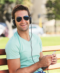 Image showing Cellphone, happy and man with headphones in park for listening to music, audio and radio. Fashion, sunglasses and person for streaming subscription, song and playlist on holiday, vacation and relax