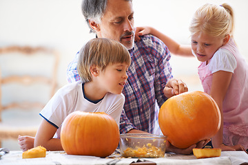 Image showing Halloween, family and carving a pumpkin with children at a home table for fun and bonding. Man or dad helping or teaching young kids with creativity, holiday lantern and craft together in a house