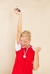 Image showing Woman, soccer player and trophy or a winner celebrate on a plain background for football achievement. A young female sports person or athlete with fist and champion medal award for winning a game