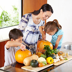 Image showing Mother, daughter and son with pumpkins for halloween in the kitchen of their home for holiday celebration. Family, food or tradition and a woman teaching her children how to carve vegetables