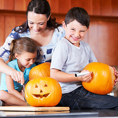 Image showing Halloween, pumpkin and a family in the kitchen of their home together for holiday celebration. Creative, smile or happy with a mother, son and daughter carving a face into a vegetable for decoration