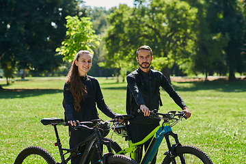 Image showing A blissful couple, adorned in professional cycling gear, enjoys a romantic bicycle ride through a park, surrounded by modern natural attractions, radiating love and happiness