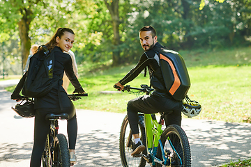 Image showing A blissful couple, adorned in professional cycling gear, enjoys a romantic bicycle ride through a park, surrounded by modern natural attractions, radiating love and happiness