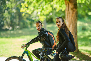 Image showing A blissful couple, adorned in professional cycling gear, enjoys a romantic bicycle ride through a park, surrounded by modern natural attractions, radiating love and happiness