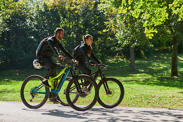 Image showing A blissful couple, adorned in professional cycling gear, enjoys a romantic bicycle ride through a park, surrounded by modern natural attractions, radiating love and happiness