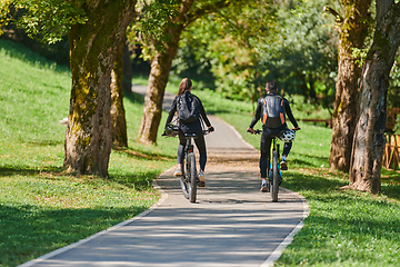 Image showing A blissful couple, adorned in professional cycling gear, enjoys a romantic bicycle ride through a park, surrounded by modern natural attractions, radiating love and happiness