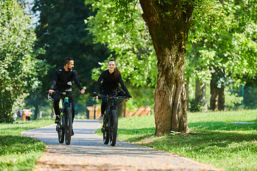 Image showing A blissful couple, adorned in professional cycling gear, enjoys a romantic bicycle ride through a park, surrounded by modern natural attractions, radiating love and happiness