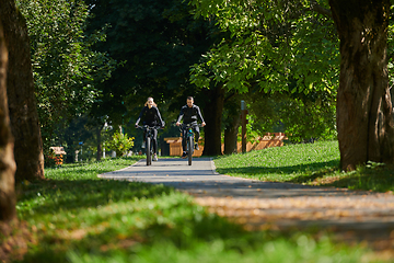 Image showing A blissful couple, adorned in professional cycling gear, enjoys a romantic bicycle ride through a park, surrounded by modern natural attractions, radiating love and happiness