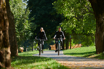 Image showing A blissful couple, adorned in professional cycling gear, enjoys a romantic bicycle ride through a park, surrounded by modern natural attractions, radiating love and happiness