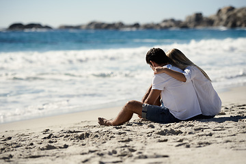 Image showing Love, embrace and couple sitting on beach for date, outdoor bonding and tropical holiday. Romance, man and woman at sea, hugging and relax on ocean vacation together with travel, care and adventure.