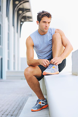 Image showing Man, fitness and tying shoes getting ready for workout, exercise or outdoor training with earphones. Active male person or athlete tie shoe on concrete bench in preparation for run or cardio outside