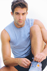 Image showing Man, portrait and tying shoes with earphones in fitness for workout or exercise against a white studio background. Active male person or athlete sitting to tie shoe in preparation for cardio training