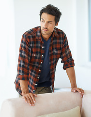 Image showing Man, thinking and serious by sofa for ideas, question and contemplating in living room of apartment or home. Person, face or thoughtful or pride by couch in lounge for chill, rest or shirt on weekend