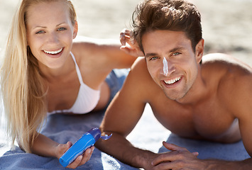 Image showing Love, portrait and sunscreen with happy couple on beach blanket for date, bonding and tropical holiday. Romance, man and woman with cream, skincare and relax together with travel and adventure.