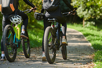 Image showing A blissful couple, adorned in professional cycling gear, enjoys a romantic bicycle ride through a park, surrounded by modern natural attractions, radiating love and happiness