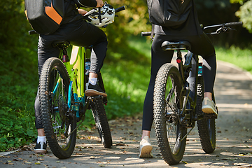 Image showing A blissful couple, adorned in professional cycling gear, enjoys a romantic bicycle ride through a park, surrounded by modern natural attractions, radiating love and happiness