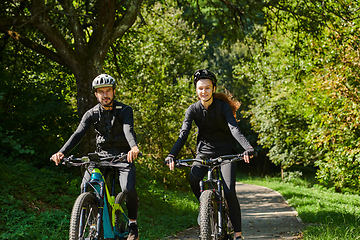 Image showing A blissful couple, adorned in professional cycling gear, enjoys a romantic bicycle ride through a park, surrounded by modern natural attractions, radiating love and happiness