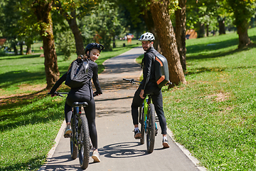 Image showing A blissful couple, adorned in professional cycling gear, enjoys a romantic bicycle ride through a park, surrounded by modern natural attractions, radiating love and happiness