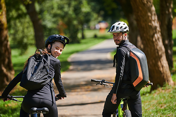 Image showing A blissful couple, adorned in professional cycling gear, enjoys a romantic bicycle ride through a park, surrounded by modern natural attractions, radiating love and happiness