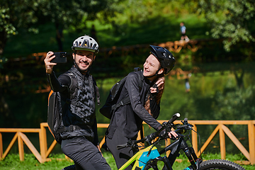 Image showing A modern couple captures the joy of their bike ride in the park through a trendy selfie, blending technology and outdoor adventure to immortalize a moment of happiness and togetherness