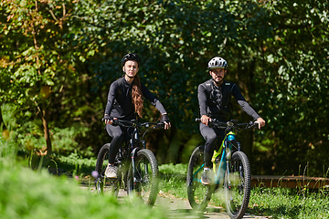 Image showing A blissful couple, adorned in professional cycling gear, enjoys a romantic bicycle ride through a park, surrounded by modern natural attractions, radiating love and happiness