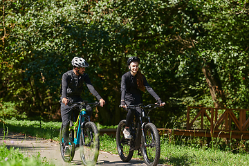 Image showing A blissful couple, adorned in professional cycling gear, enjoys a romantic bicycle ride through a park, surrounded by modern natural attractions, radiating love and happiness