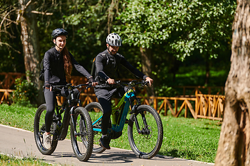 Image showing A blissful couple, adorned in professional cycling gear, enjoys a romantic bicycle ride through a park, surrounded by modern natural attractions, radiating love and happiness