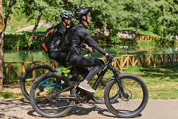 Image showing A blissful couple, adorned in professional cycling gear, enjoys a romantic bicycle ride through a park, surrounded by modern natural attractions, radiating love and happiness