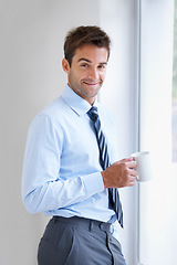 Image showing Portrait, smile and coffee with a business man by a window in the office at the start of his work day. Corporate, company and career with a happy young employee drinking tea in the workplace