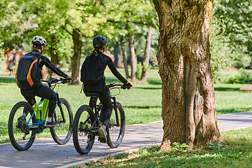 Image showing A blissful couple, adorned in professional cycling gear, enjoys a romantic bicycle ride through a park, surrounded by modern natural attractions, radiating love and happiness