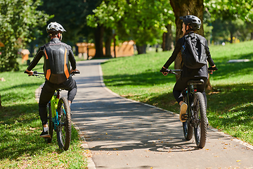 Image showing A blissful couple, adorned in professional cycling gear, enjoys a romantic bicycle ride through a park, surrounded by modern natural attractions, radiating love and happiness