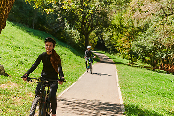 Image showing A blissful couple, adorned in professional cycling gear, enjoys a romantic bicycle ride through a park, surrounded by modern natural attractions, radiating love and happiness