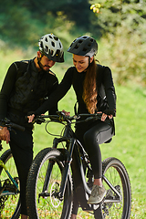 Image showing A blissful couple, adorned in professional cycling gear, enjoys a romantic bicycle ride through a park, surrounded by modern natural attractions, radiating love and happiness