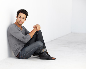 Image showing Handsome, fashion and young man by a white wall with casual, cool and trendy outfit. Attractive, confidence and serious male model from Canada sitting on floor with edgy style for aesthetic.