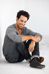 Image showing Smile, fashion and handsome young man by white wall with casual, cool and trendy outfit. Happy, confident and attractive male model from Canada sitting on floor with edgy style and positive attitude.