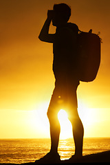 Image showing Silhouette, man and hiking at ocean with sunset, backpack and scenery for holiday or vacation is summer. Shadow, person and relaxing with view, adventure and hiker for recreation, travel or sun flare