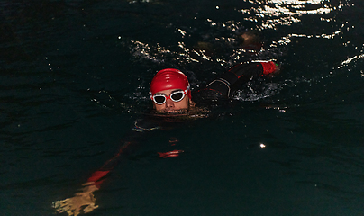 Image showing A determined professional triathlete undergoes rigorous night time training in cold waters, showcasing dedication and resilience in preparation for an upcoming triathlon swim competition