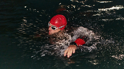 Image showing A determined professional triathlete undergoes rigorous night time training in cold waters, showcasing dedication and resilience in preparation for an upcoming triathlon swim competition