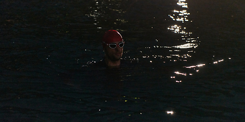 Image showing A determined professional triathlete undergoes rigorous night time training in cold waters, showcasing dedication and resilience in preparation for an upcoming triathlon swim competition