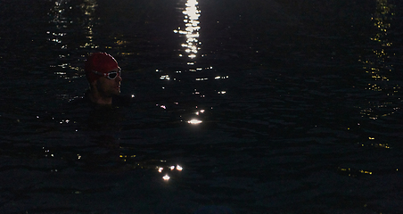 Image showing A determined professional triathlete undergoes rigorous night time training in cold waters, showcasing dedication and resilience in preparation for an upcoming triathlon swim competition