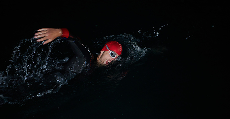 Image showing A determined professional triathlete undergoes rigorous night time training in cold waters, showcasing dedication and resilience in preparation for an upcoming triathlon swim competition