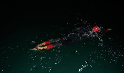 Image showing A determined professional triathlete undergoes rigorous night time training in cold waters, showcasing dedication and resilience in preparation for an upcoming triathlon swim competition