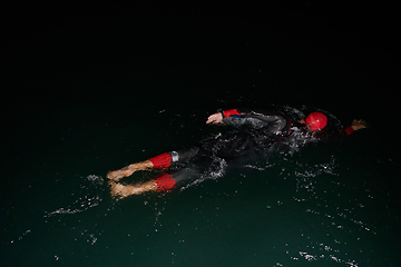 Image showing A determined professional triathlete undergoes rigorous night time training in cold waters, showcasing dedication and resilience in preparation for an upcoming triathlon swim competition